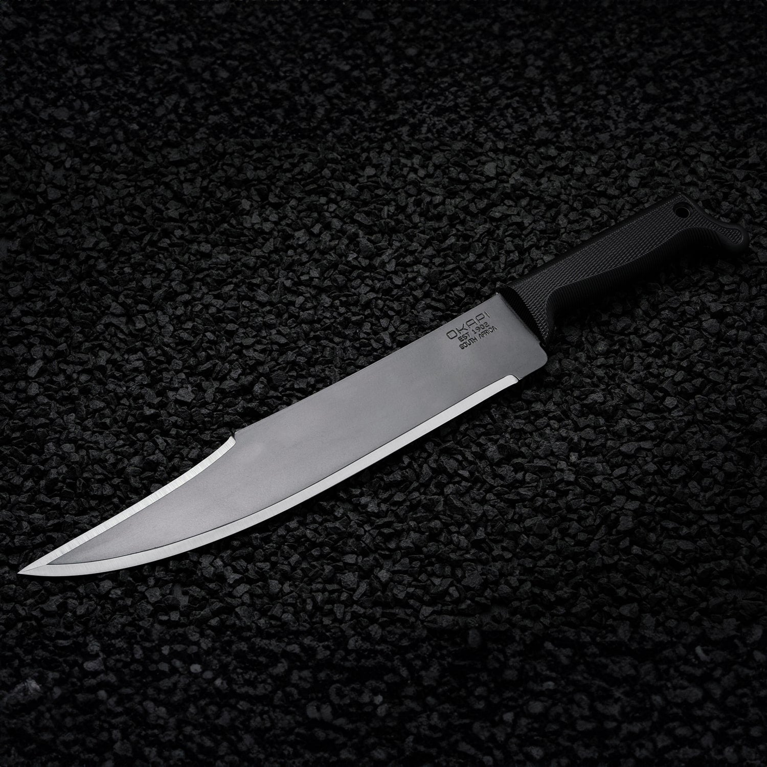 Okapi Bowie machete featuring Tactical Black handle shown on black stone ground