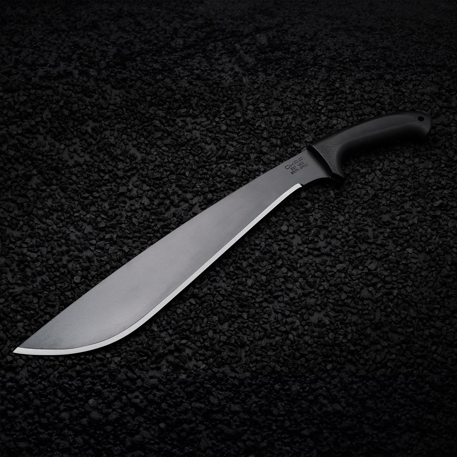 Tactical Okapi Jungle machete resting on black rock floor in lifestyle scene