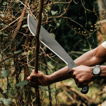 Outdoor photo of Okapi Jungle machete with black tactical handle on earthy terrain