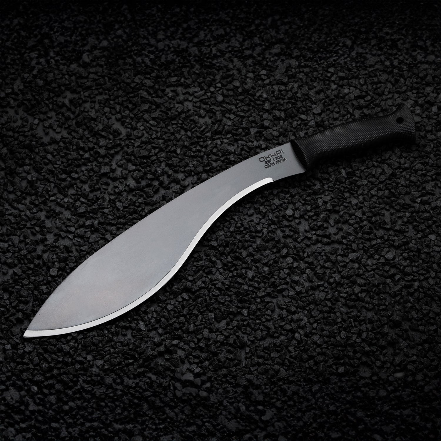 Curved Okapi Kukri machete with black grip featured on rugged rock floor scene