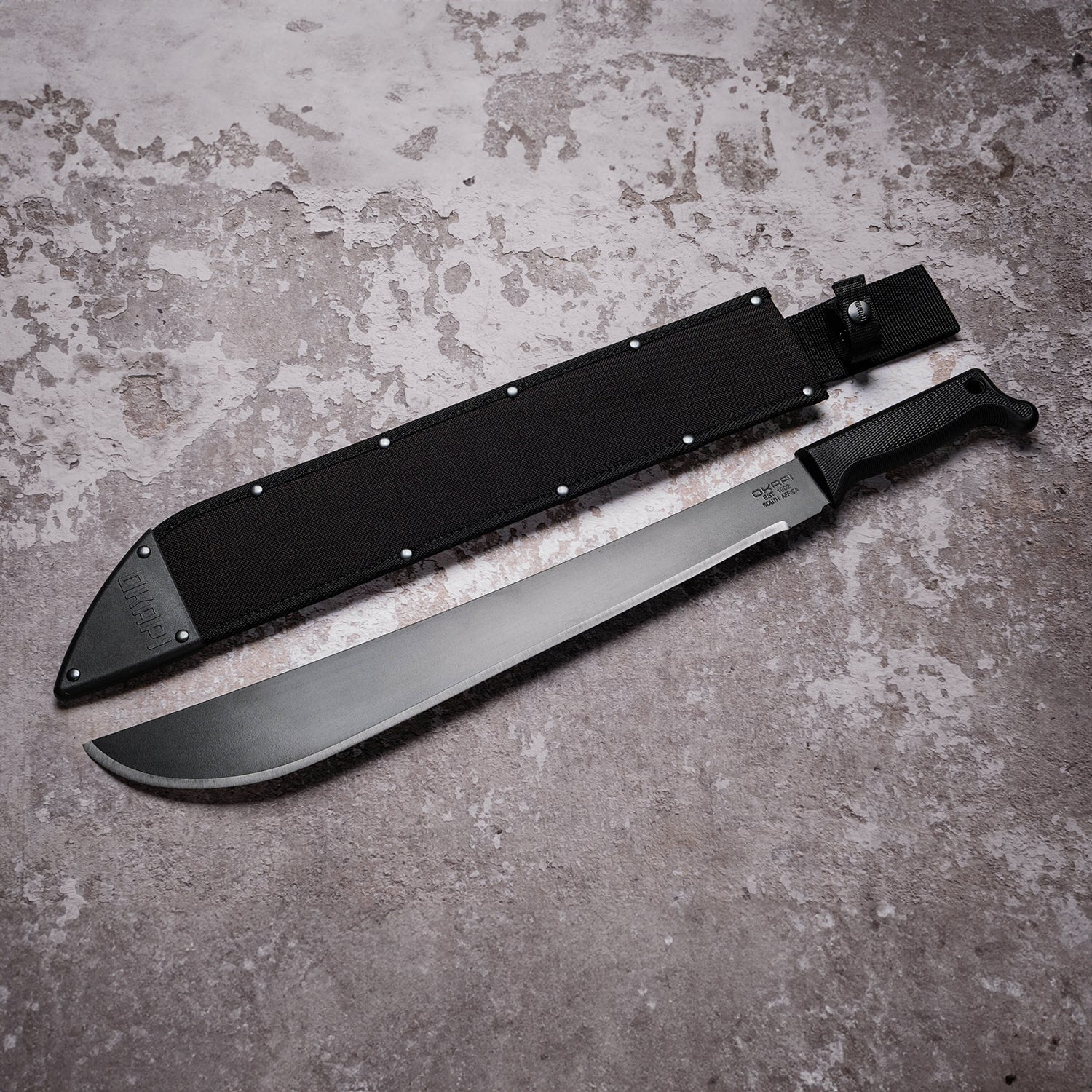 Okapi Latin machete with black tactical handle and sheath in outdoor setting
