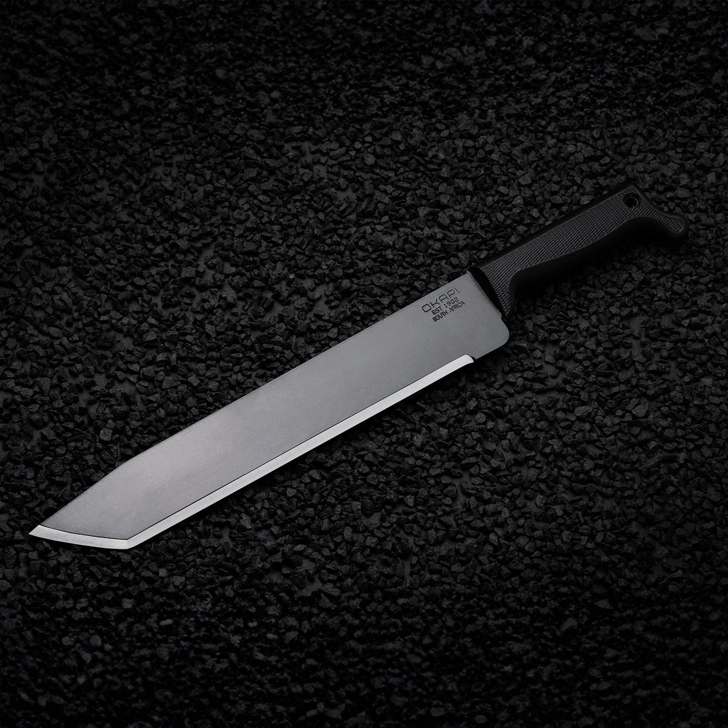 Tanto-style Okapi machete featuring a Tactical Black handle on black stone floor