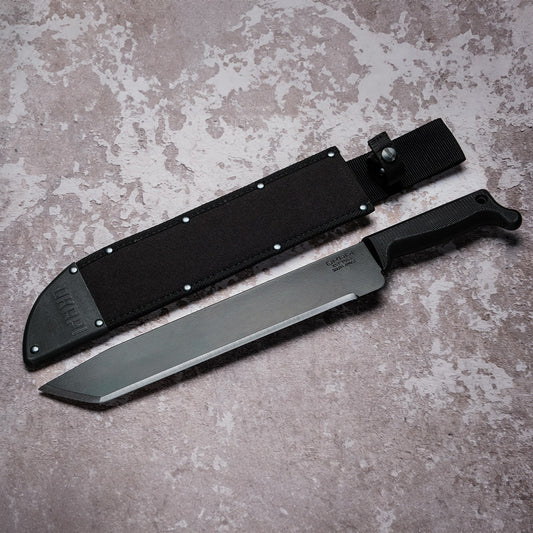 Okapi O-Tanto machete with canvas sheath resting on rugged grey stone floor