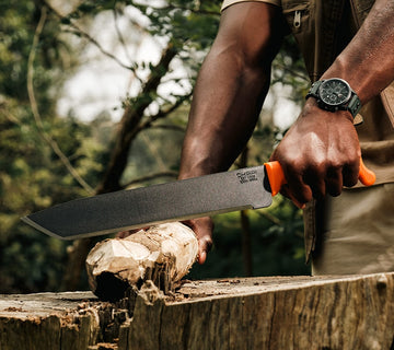 Heavy-duty Okapi machete with tanto-style blade and Okapi Orange handle on earthy terrain