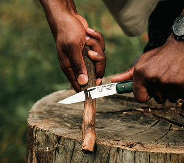 Okapi utility folding knife with green grip shown in rugged, natural environment