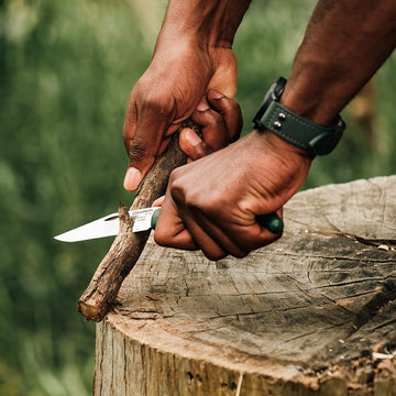 Okapi folding knife with durable green handle resting on wooden block outdoors